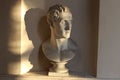 Closeup of a bust of Napoleon near a sunlit wall statue in a chamber of Mantova