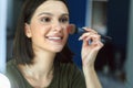 Closeup candid portrait of a happy brunette young woman looking to the mirror and making makeup herself Royalty Free Stock Photo