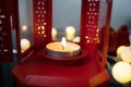 Closeup candle with fire flame in red Christmas lantern on table near fairy lights