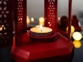 Closeup candle with fire flame in red Christmas lantern on table near fairy lights