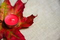 Closeup candle on a multi-colored maple leaf on linen fabric. Selective Focus, top view, flat lay. Autumn composition background