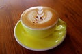 Closeup cappuccino coffee with latte art in a yellow cup on wooden table Royalty Free Stock Photo