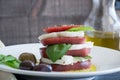 Closeup Caprese Salad with sliced red tomato, buffalo mozzarella, basil leaves and healthy whole olives dripping in extra virgin o Royalty Free Stock Photo