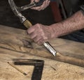 Closeup of carpenter`s rough hands chiseling wood board using hammer