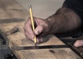 Closeup of carpenter`s rough hands using a pencil and old square to mark a line on a wooden board to saw Royalty Free Stock Photo