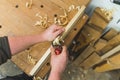 Closeup carpenter shaving a wooden board with a hand planer, wooden chips on the table