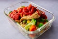 Closeup of a casserole of vegetables with chicken breast and sauce on a white surface