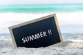 Closeup of a chalkboard with the text summer written on the sand of a beach.