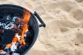 Closeup on charcoal burning with a yellow flame in a metallic barbeque on a sandy beach Royalty Free Stock Photo