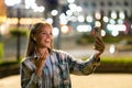 Closeup cheerful girl taking selfie photo by mobile phone on night city street. Portrait of happy woman showing victory sign to Royalty Free Stock Photo