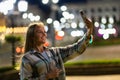 Closeup cheerful girl taking selfie photo by mobile phone on night city street. Portrait of happy woman showing victory sign to Royalty Free Stock Photo