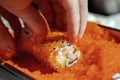 Closeup of chef hands rolling up sushi in flying fish roe (Tobiko) red caviar - focus on the roll Royalty Free Stock Photo