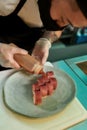 Closeup of chef in protective mask and gloves adding sauce on top of sliced tuna sushi served on a plate while preparing Royalty Free Stock Photo