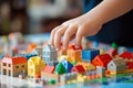 Closeup on child\'s hand placing miniature houses among colorful building blocks on a vibrant setup