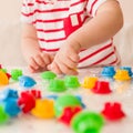 Closeup of child`s hand taking bright mosaic parts. Playing and learning colors at home. Toddler boy in a striped shirt