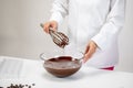 Closeup chocolatier pouring dark melted chocolate with whisk on white background