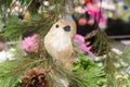 Closeup of Christmas straw bird perched on an artificial tree with pine cones with pink and colorful bokeh background