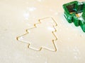 A closeup of a Christmas tree cutout in sugar cookie dough with flour and green plastic stencil or cookie cutter laying on top of