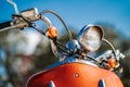 Closeup chrome detail and headlamp of orange retro vintage scooter under blue sky and sun on the blurred background. Royalty Free Stock Photo