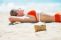 Closeup on coconut and young woman laying on beach in background