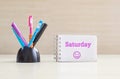 Closeup color pen with black ceramic desk tidy for pen and purple saturday word in white page and happy face emotion at the note b Royalty Free Stock Photo