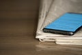 Closeup of color stacked newspapers on a wooden table background with mobile phone