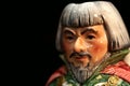 Closeup of a colorful ceramic small Chinese statue of a person against a dark blurry background Royalty Free Stock Photo