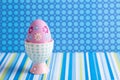 Closeup colorful painted Easter egg in vibrant modern egg stand on spotted and striped blue background