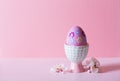 Closeup colorful painted Easter egg in vibrant modern egg stand surrounded by white flowering tree branches on pastel pink