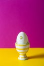 Closeup colorful painted Easter egg in vibrant modern egg stand surrounded by white flowering tree branches on vibrant crimson and