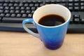 Closeup of computer keyboard, blue large cup of coffee, tea suddenly spills, hot liquid spoils equipment, concept of tea time, Royalty Free Stock Photo