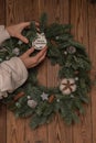 Closeup coniferous holiday wreath on a wooden door. Woman faceless affix inscription Merry Christmas.