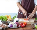 Closeup The cook`s hand is slicing vegetables. on a wooden chopping board with a knife on the kitchen table filled with vegetables Royalty Free Stock Photo