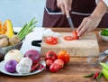 Closeup The cook`s hand is slicing vegetables. on a wooden chopping board with a knife on the kitchen table filled with vegetables Royalty Free Stock Photo