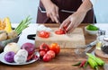 Closeup The cook`s hand is slicing vegetables. on a wooden chopping board with a knife on the kitchen table filled with vegetables Royalty Free Stock Photo