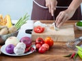 Closeup The cook`s hand is slicing vegetables. on a wooden chopping board with a knife on the kitchen table filled with vegetables Royalty Free Stock Photo