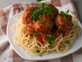 Closeup cooked spaghetti with meatballs in tomato sauce on a checkered cotton table-napkin on wooden background