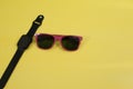 Closeup of cool purple summer sunglasses and a black smartwatch isolated on a yellow background