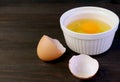 Cracked eggshell on dark brown wooden table with blurry raw egg bowl in background Royalty Free Stock Photo