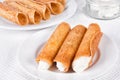 Closeup of cream filled brandy snaps, unfilled snaps, and a pot with cream