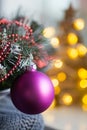 Closeup crimson Christmas ball on fir branch with warm bokeh lights on background.