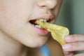 Crop anonymous girl biting crunchy potato chip at home