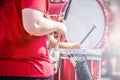 Closeup crop of girl in red tee shirt playing the drums in marching band with blurred drummer behind and lens flare