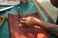 Closeup and crop hands of leather craftsman sewing a leather brown bag for a customer