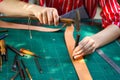 Closeup and crop hands of young female leather maker using a small hummer with leather punching steel to make a leather belt for