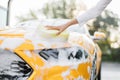 Closeup cropped image of hand of caucasian woman with yellow sponge washing hood and headlights Royalty Free Stock Photo