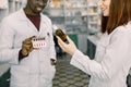 Closeup cropped portrait of two smiling friendly pharmacists working in modern farmacy. African man holds red pills Royalty Free Stock Photo