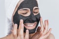 Closeup cropped portrait of young happy female applying facial cosmetic black clay organic mask on her face, wears white towel on Royalty Free Stock Photo