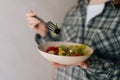 Closeup cropped shot of unrecognizable woman with fork eating fresh salad at home kitchen with light interior. Beautiful Royalty Free Stock Photo