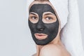 Closeup cropped studio portrait of amazed young woman with black clay organic mask on her face, wears white towel on hair. Female Royalty Free Stock Photo